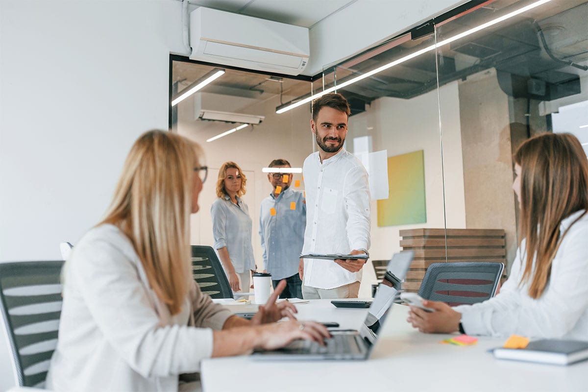 Un team di professionisti che analizza documenti e procedure scritte attorno a un tavolo in un ufficio moderno, con un laptop e note colorate.